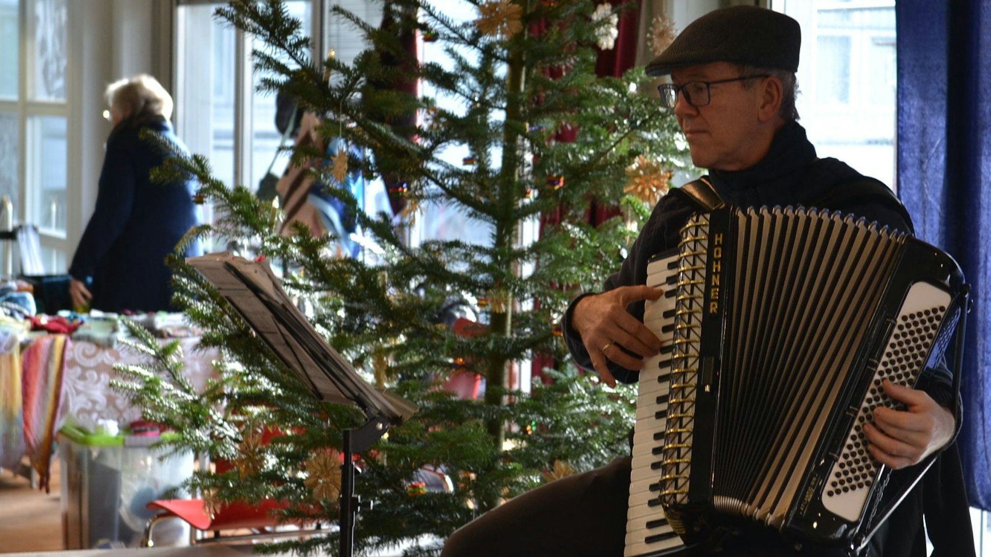 Ein Musiker spielt vor einem geschmückten Weihnachtsbaum auf dem Akkordeon.