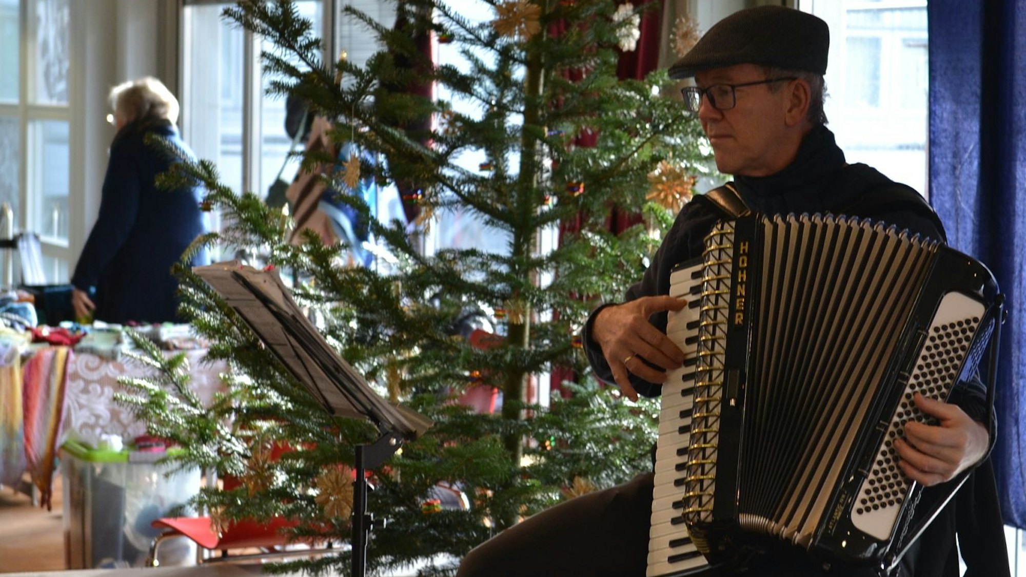 Ein Musiker spielt vor einem geschmückten Weihnachtsbaum auf dem Akkordeon.