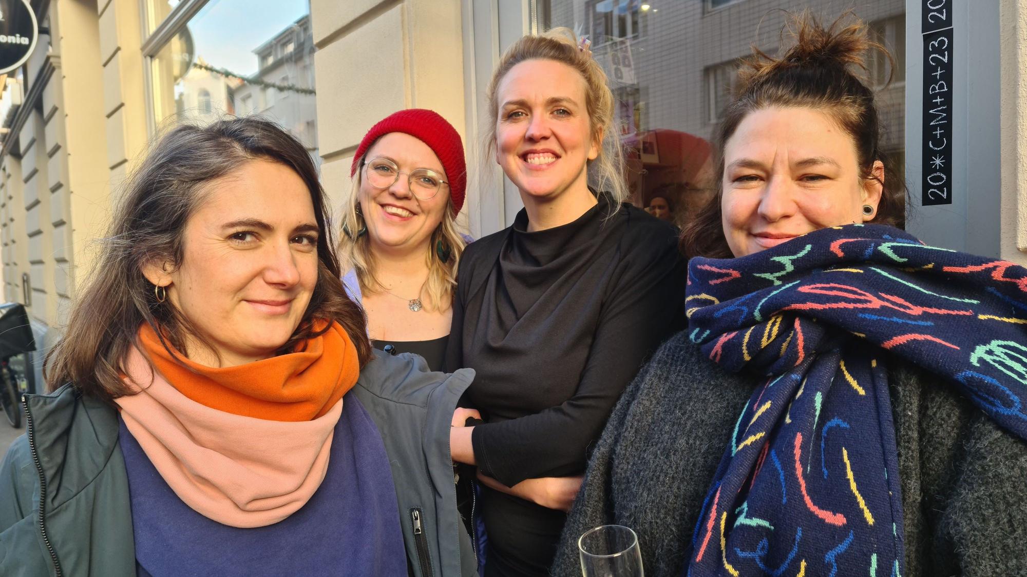Vier Frauen stehen vor einer Ladenfront. Alles vier lachen selbstbewusst in die Kamera.