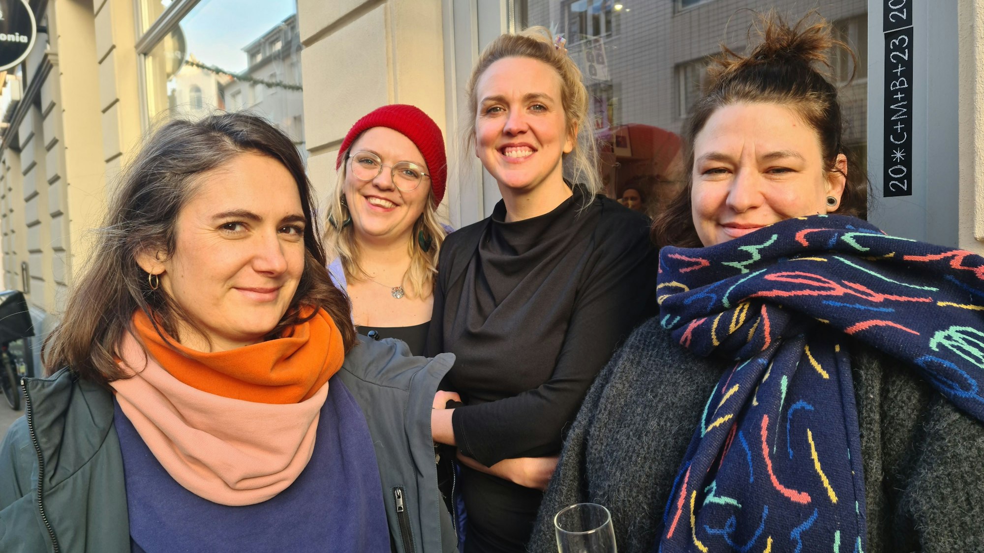Vier Frauen stehen vor einer Ladenfront. Alles vier lachen selbstbewusst in die Kamera.