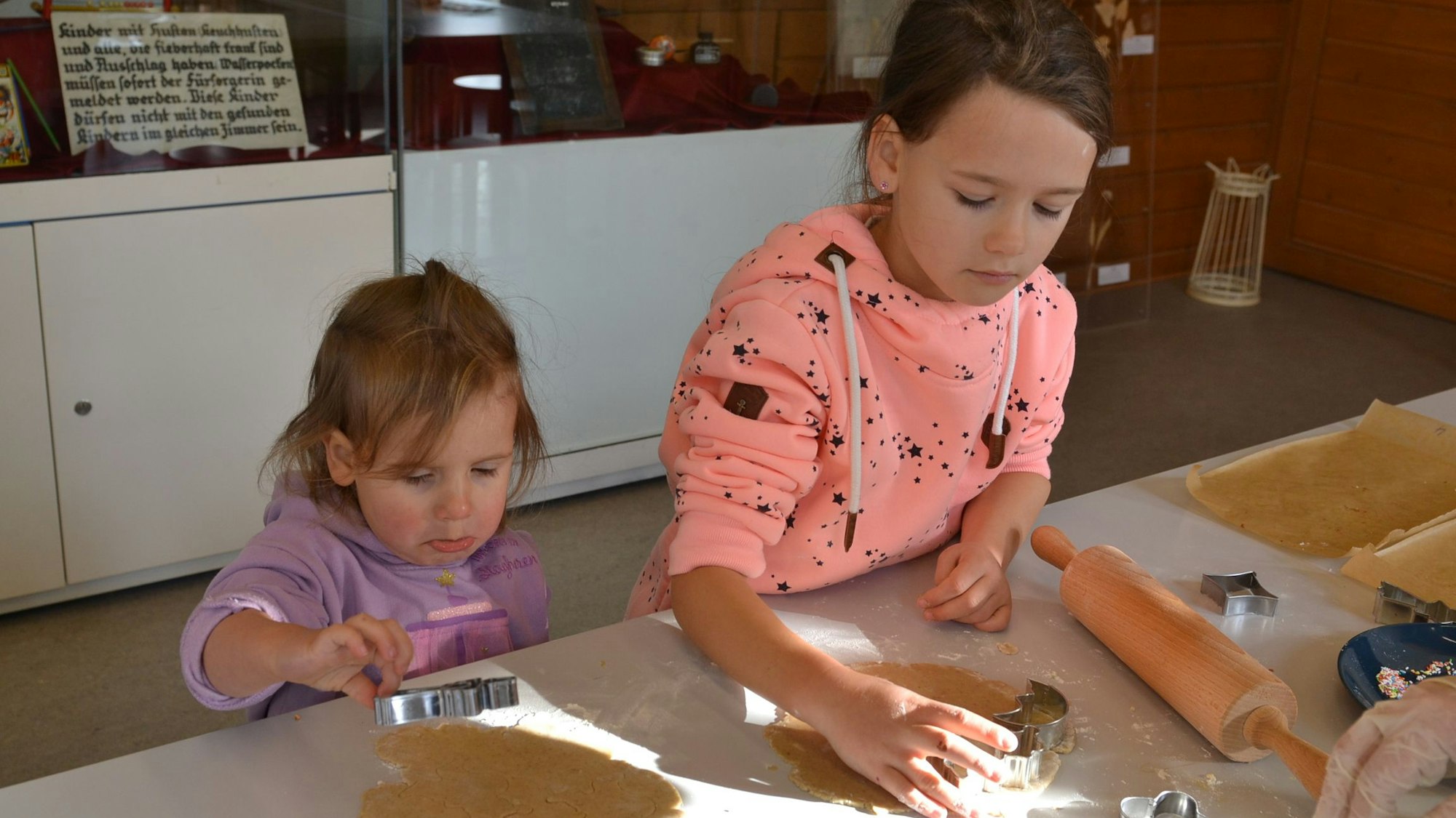 Zwei Mädchen stechen hochkonzentriert Plätzchen aus dem ausgerollten Teig.