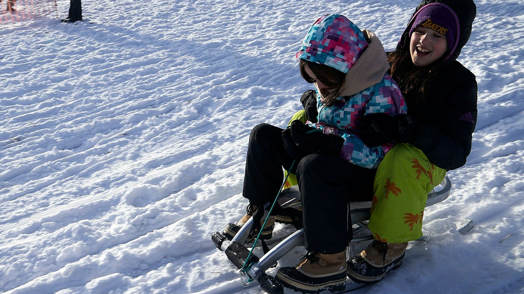 Die beiden Kinder sausen auf einem Schlitten durch den Schnee.