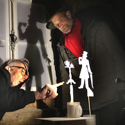 Zwei Männer begutachten eine kleine, aus Papier ausgeschnittene Figur