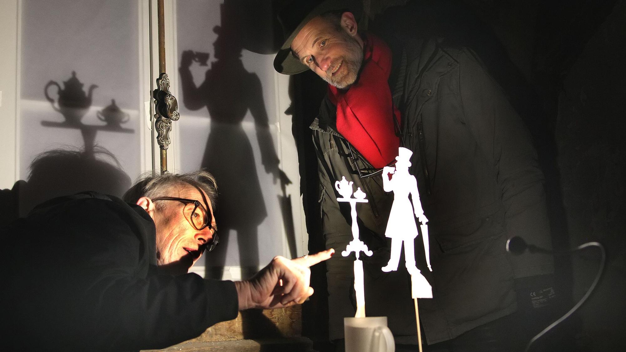 Zwei Männer begutachten eine kleine, aus Papier ausgeschnittene Figur