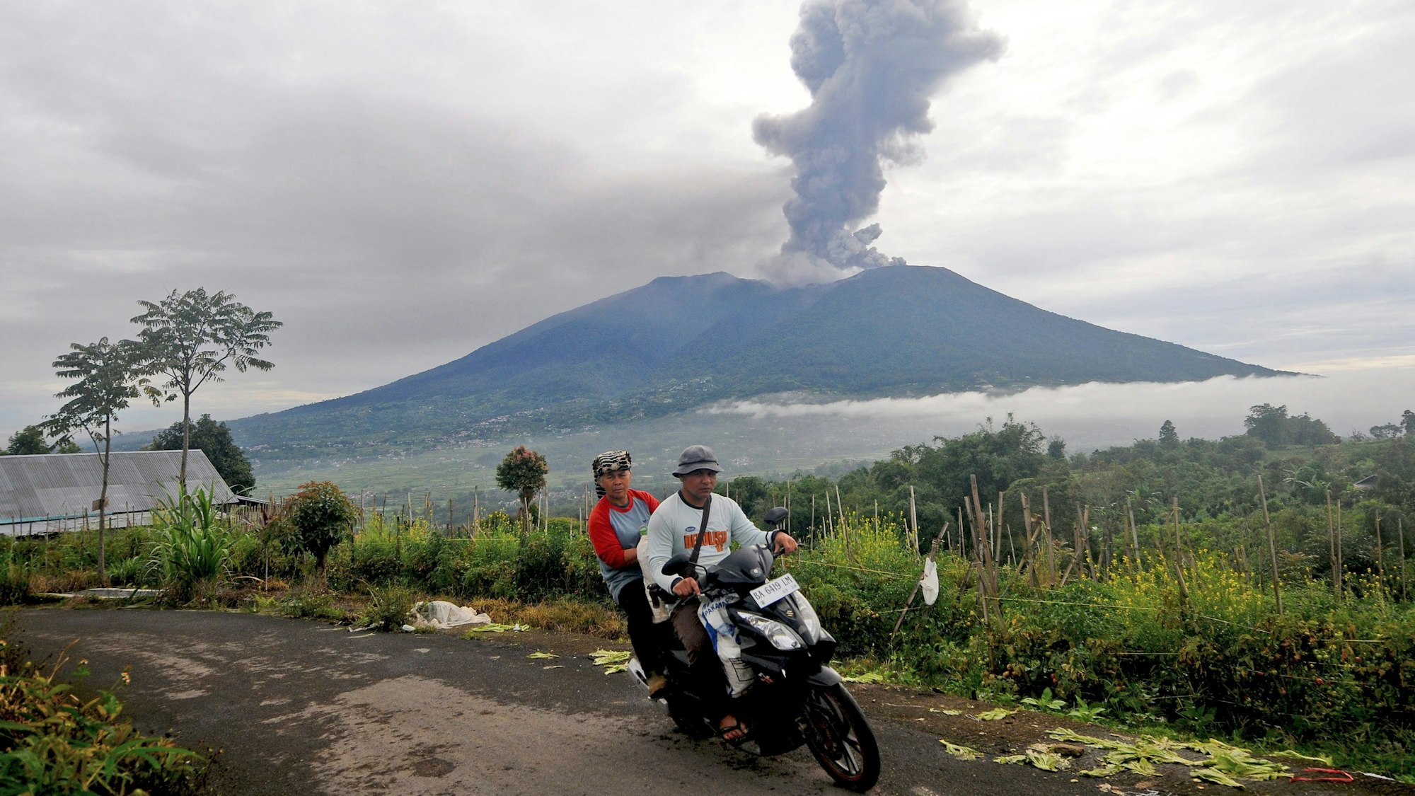 04.12.2023, Indonesien, Agam: Rollerfahrer fahren vorbei, als der Berg Marapi im Hintergrund während eines Ausbruchs vulkanisches Material ausspuckt. Foto: Ardhy Fernando/AP +++ dpa-Bildfunk +++