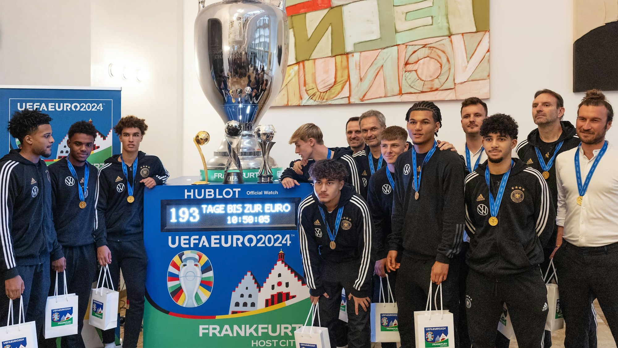 Junge Männer in dunklen Trainingsanzügen posieren um einen großen Pokal.