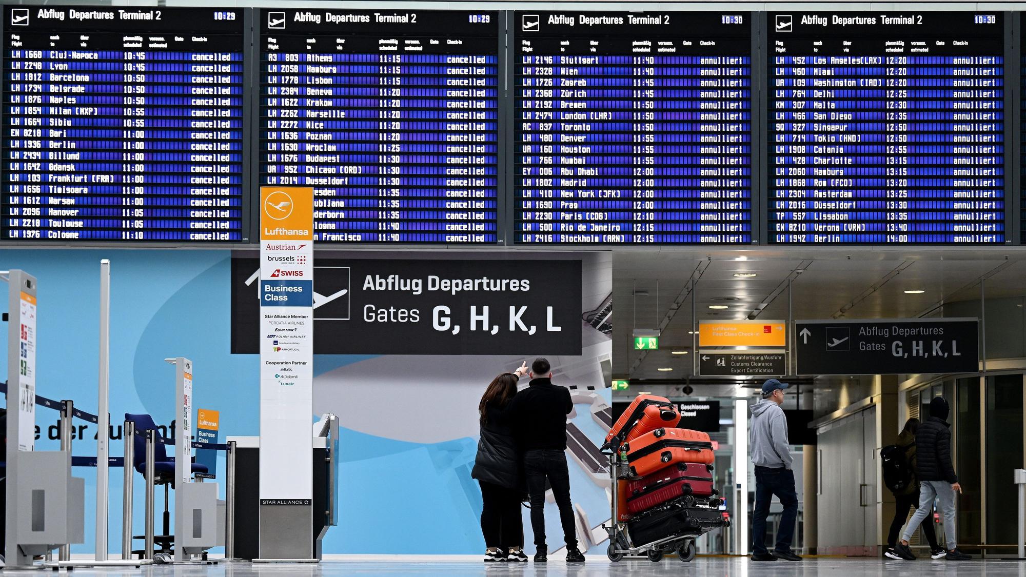 Passagiere stehen im Münchner Flughafen vor der Anzeigentafel. Wegen eines angekündigten Eisregens wird es am Münchner Flughafen am Dienstag von Betriebsbeginn bis 12 Uhr keine Starts und Landungen geben.