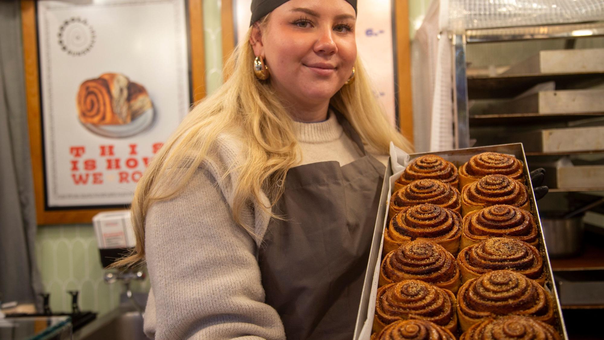 Eine blonde Frau zeigt ein Blech Zimtschnecken.