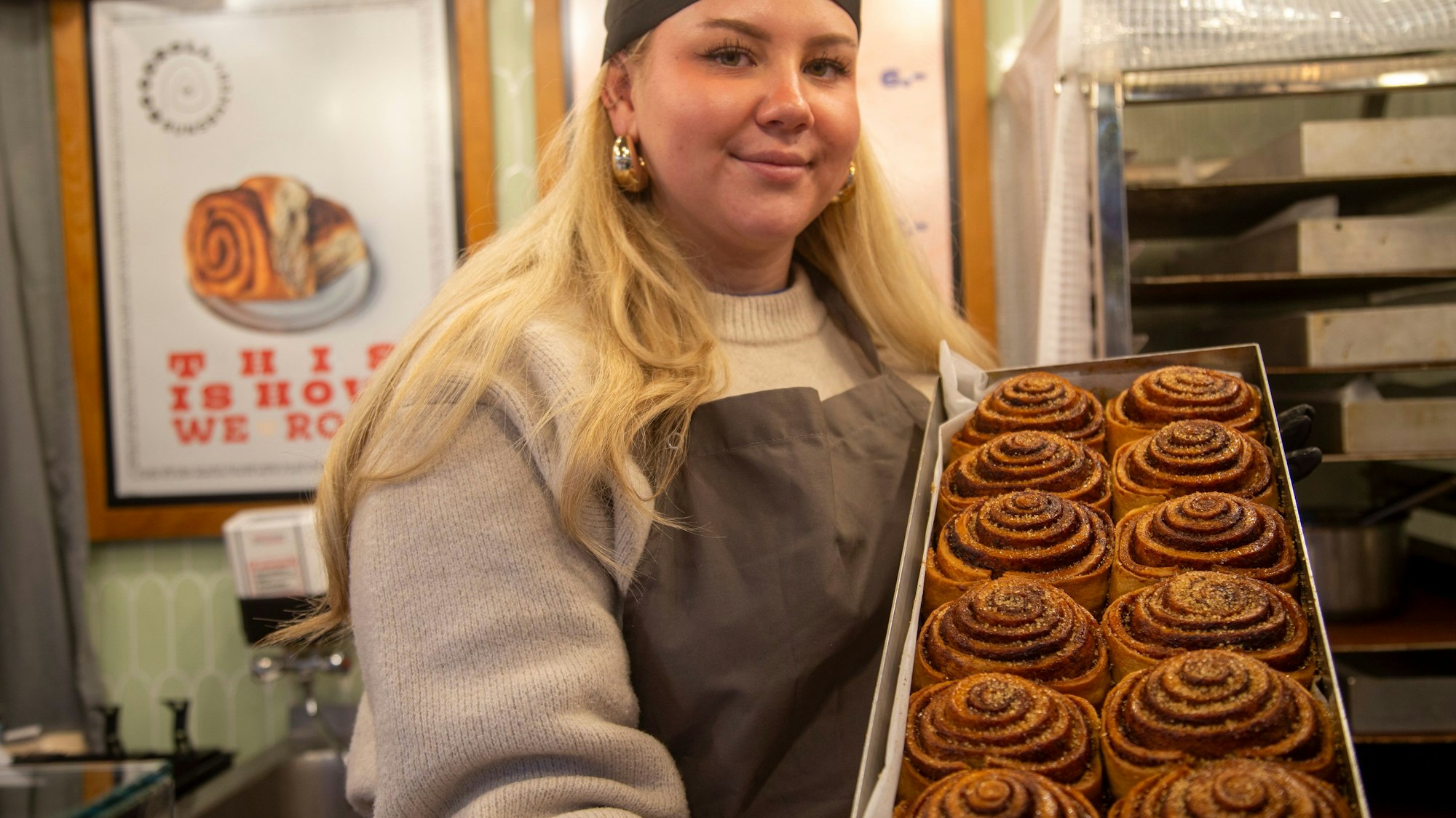 Eine blonde Frau zeigt ein Blech Zimtschnecken.