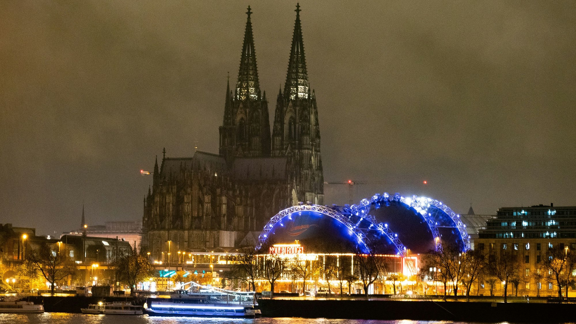 Der Musical Dome neben dem Kölner Dom ist bei Nacht blau angestrahlt.