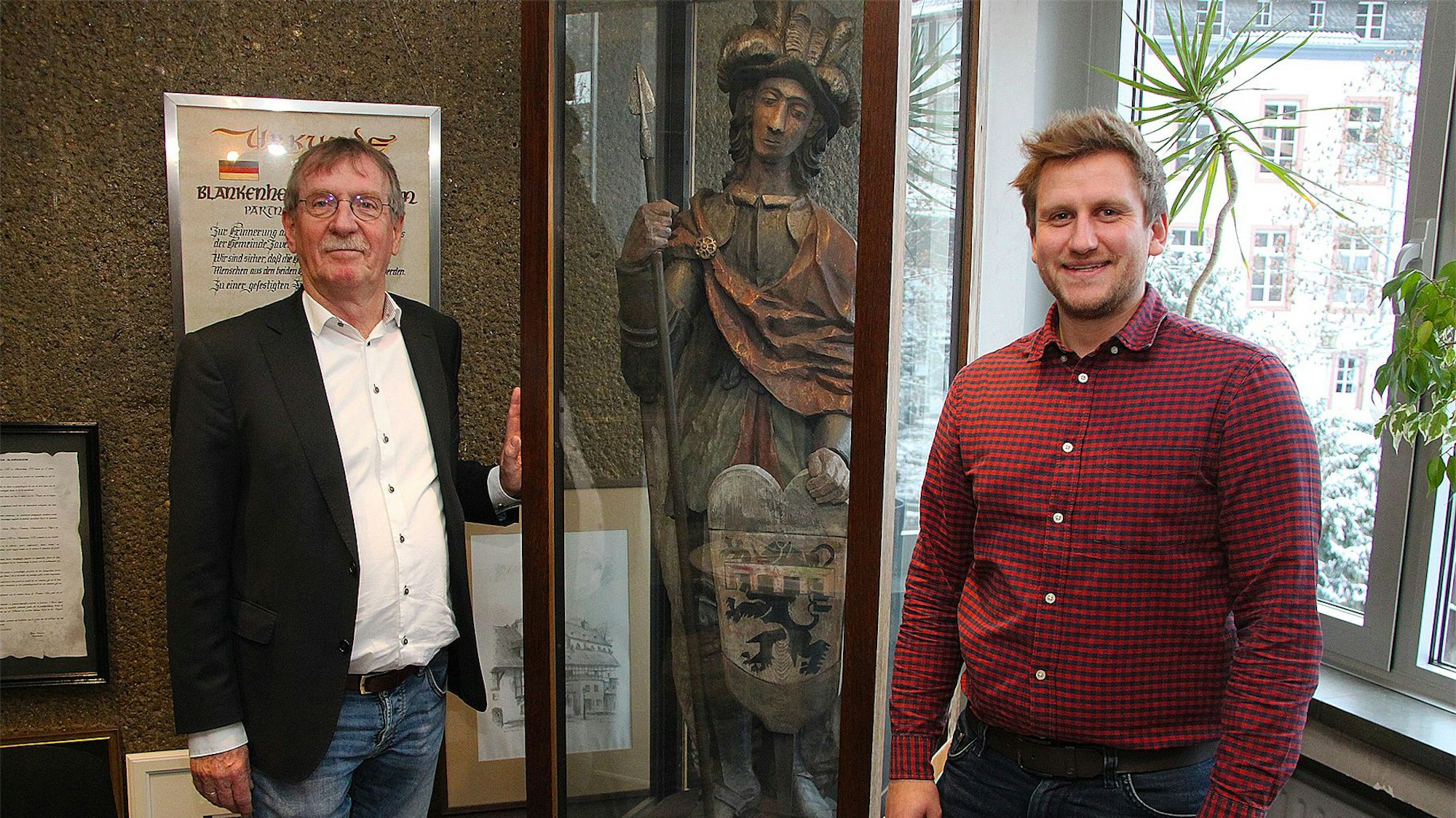 Erwin Nelles (links) und Robin Poensgen stehen an der Vitrine im Blankenheimer Rathaus, in der die Figur des heiligen Nepomuk mit dem Wappen aufbewahrt wird.