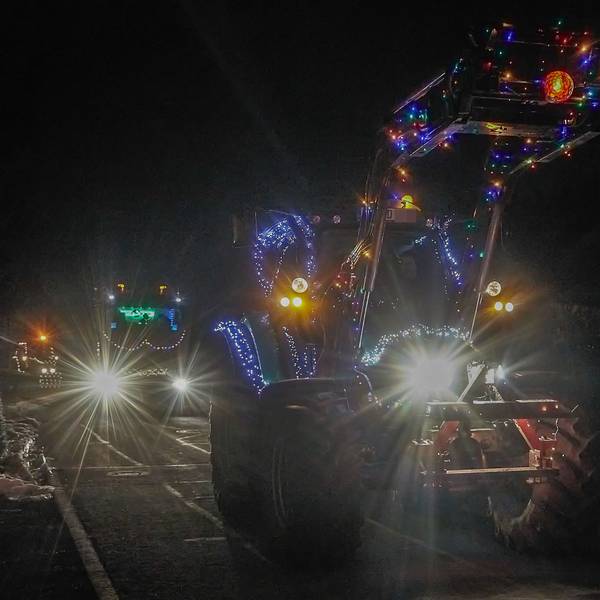 Ein beleuchteter Traktor fährt durch ein Dorf.