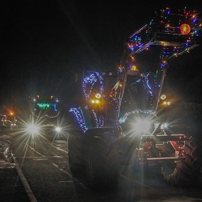 Ein beleuchteter Traktor fährt durch ein Dorf.