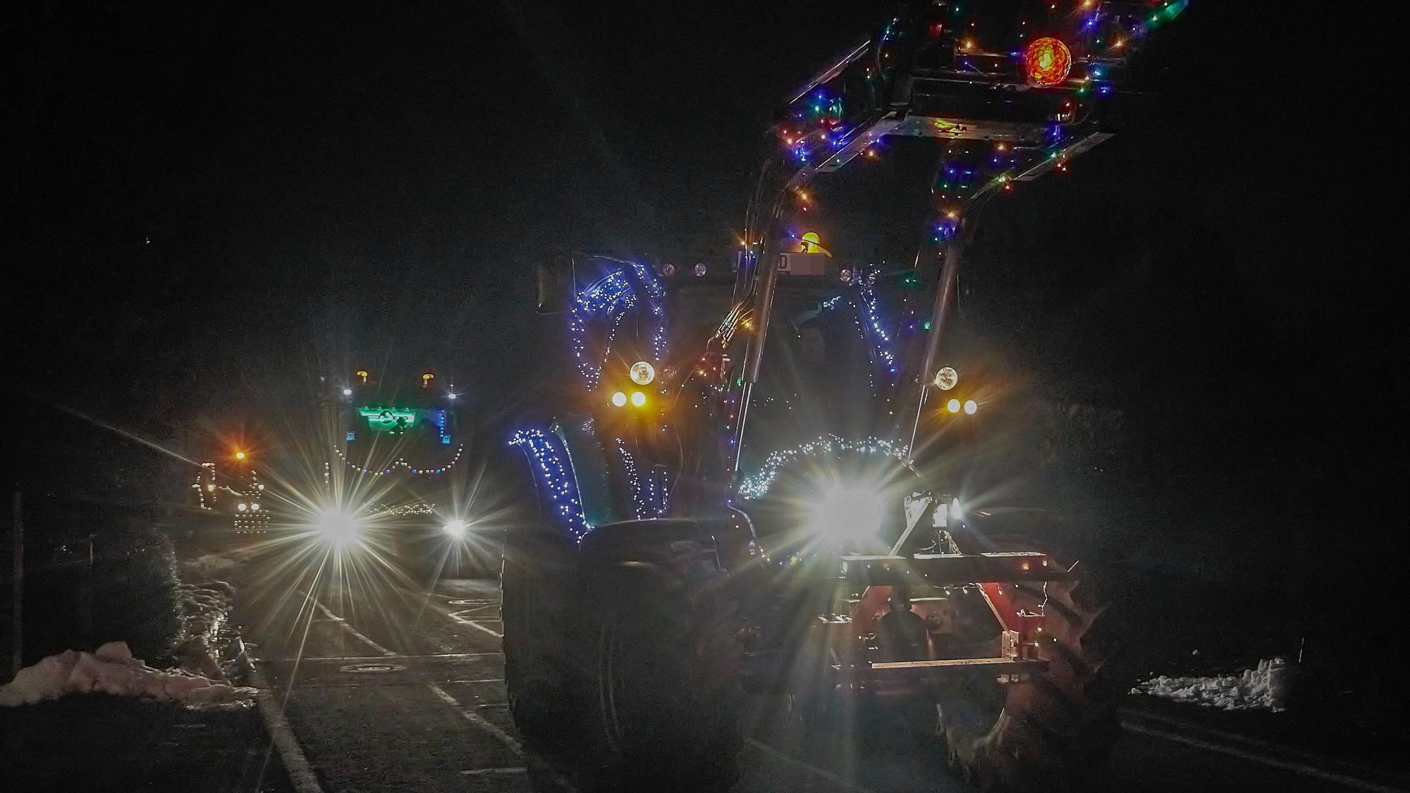 Ein beleuchteter Traktor fährt durch ein Dorf.
