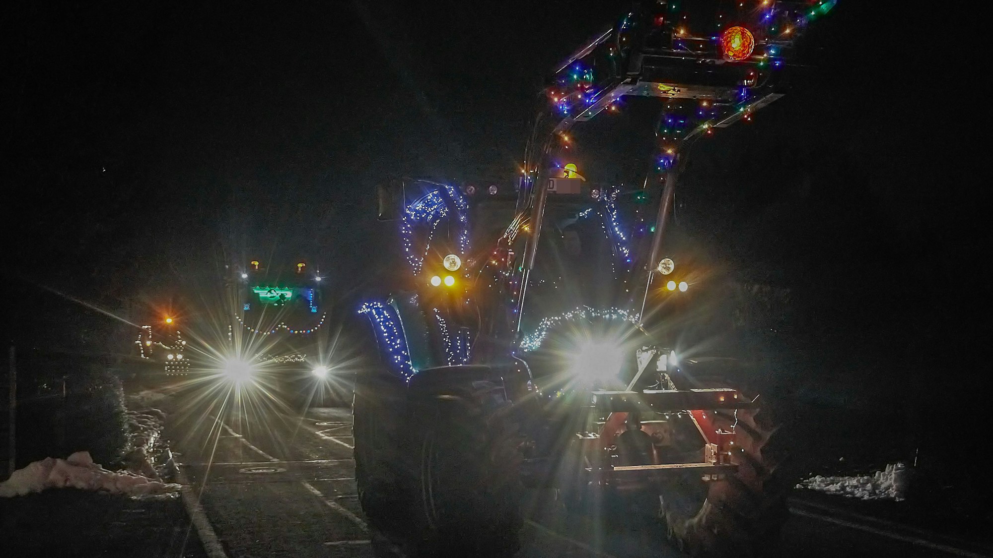 Ein beleuchteter Traktor fährt durch ein Dorf.