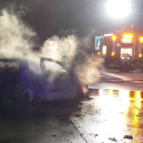 Das Foto zeigt den ausgebrannten Wagen und ein Einsatzfahrzeug der Feuerwehr auf der Autobahn.