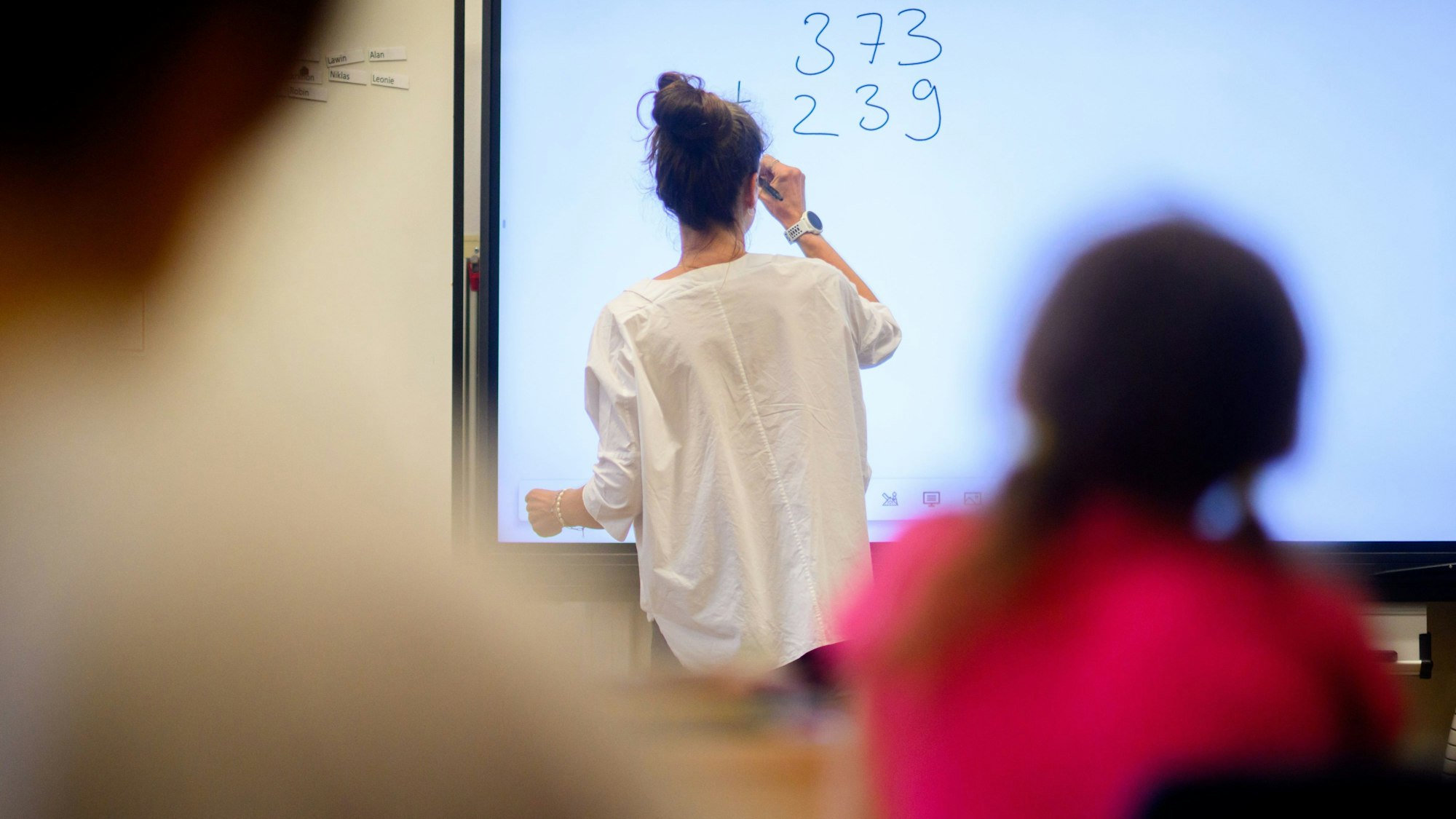 Ein Lehrerin schreibt eine Mathematikaufgabe auf eine digitale Schultafel im Klassenraum.