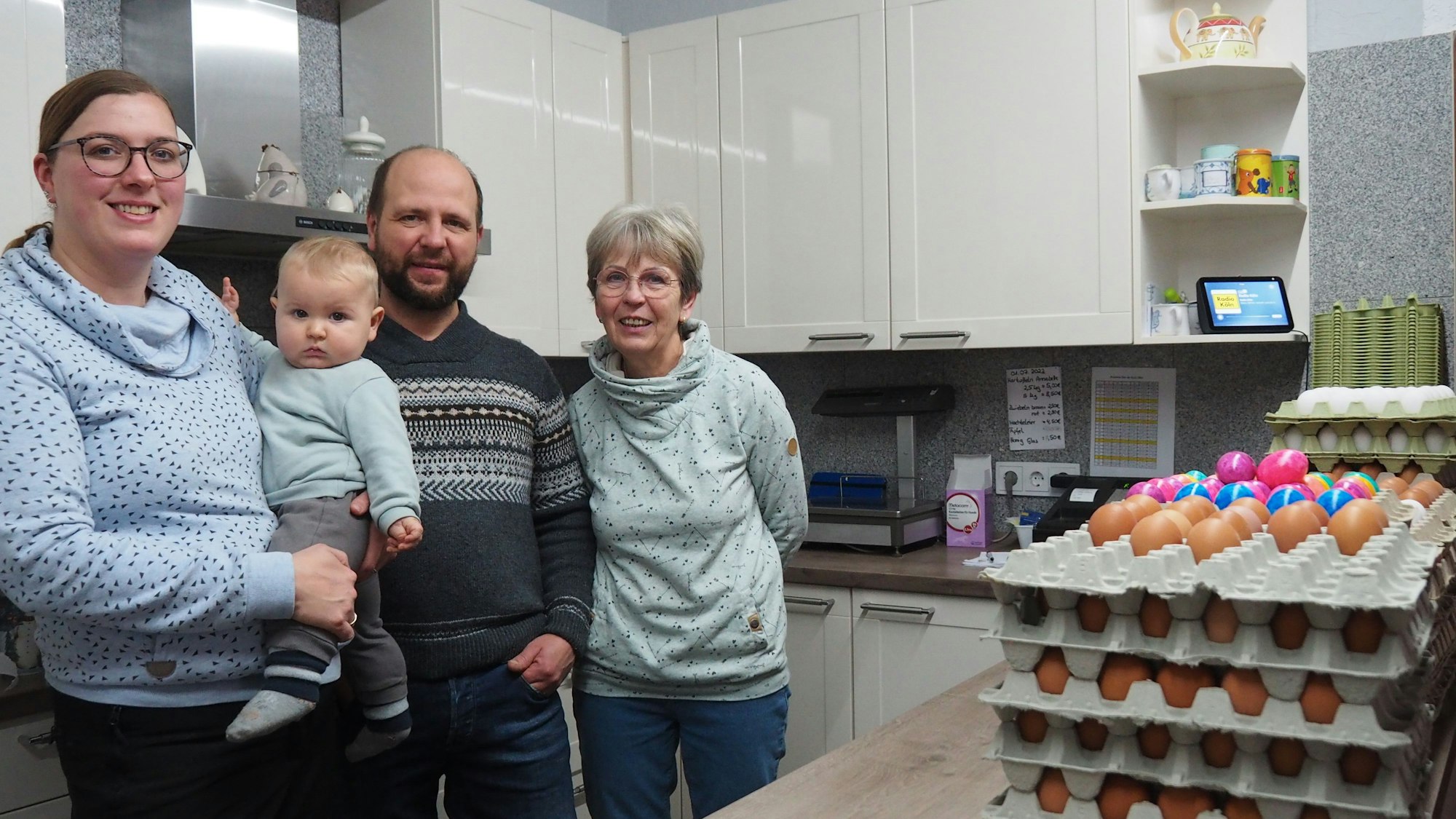 Eine junge Frau hat ein Baby auf dem Arm, daneben stehen ein Mann mit Bart und eine ältere Dame.