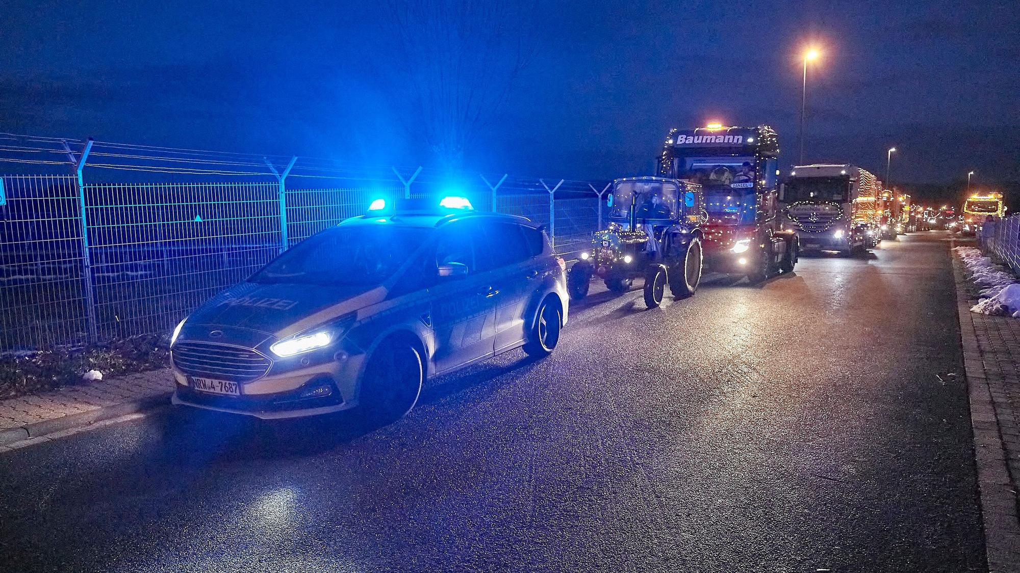 Ein Konvoi mit beleuchteten Traktoren wird von einem Polizeiwagen angeführt.