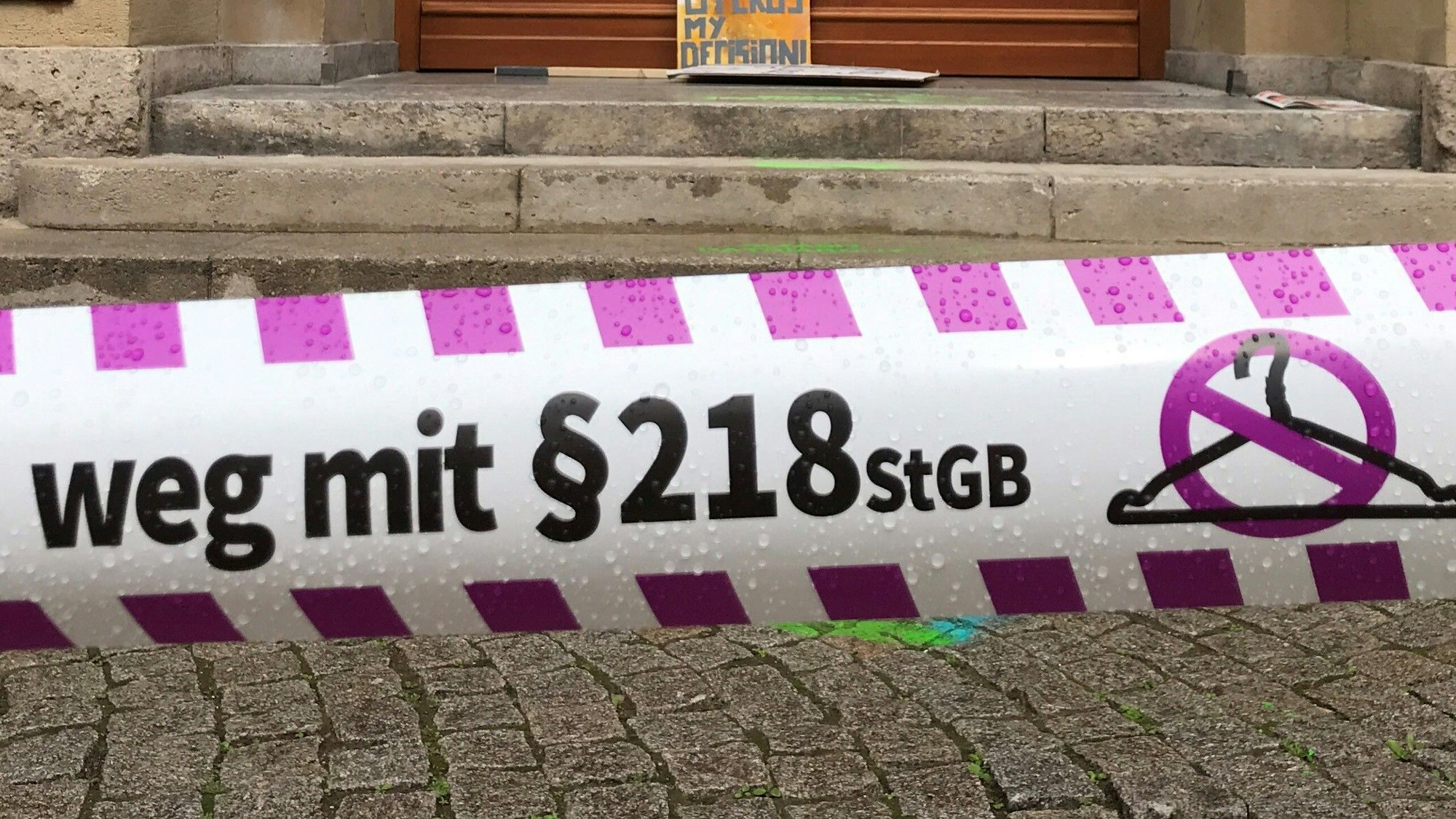 Ein Absperrband mit dem Aufdruck „Weg mit §218 StGB“ hängt vor einem Gebäude.
