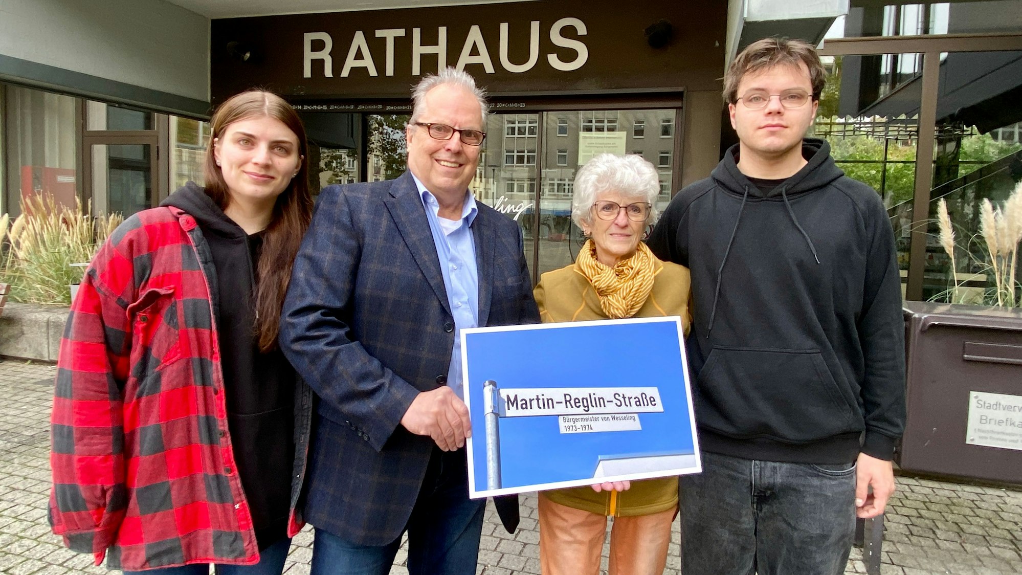 Vier Personen, zwei Frauen und zwei Männer stehen vor dem Wesselinger Rathaus. In der Hand halten die beiden Personen in der Mitte ein Bild mit dem Schild der Martin-Reglin-Straße.