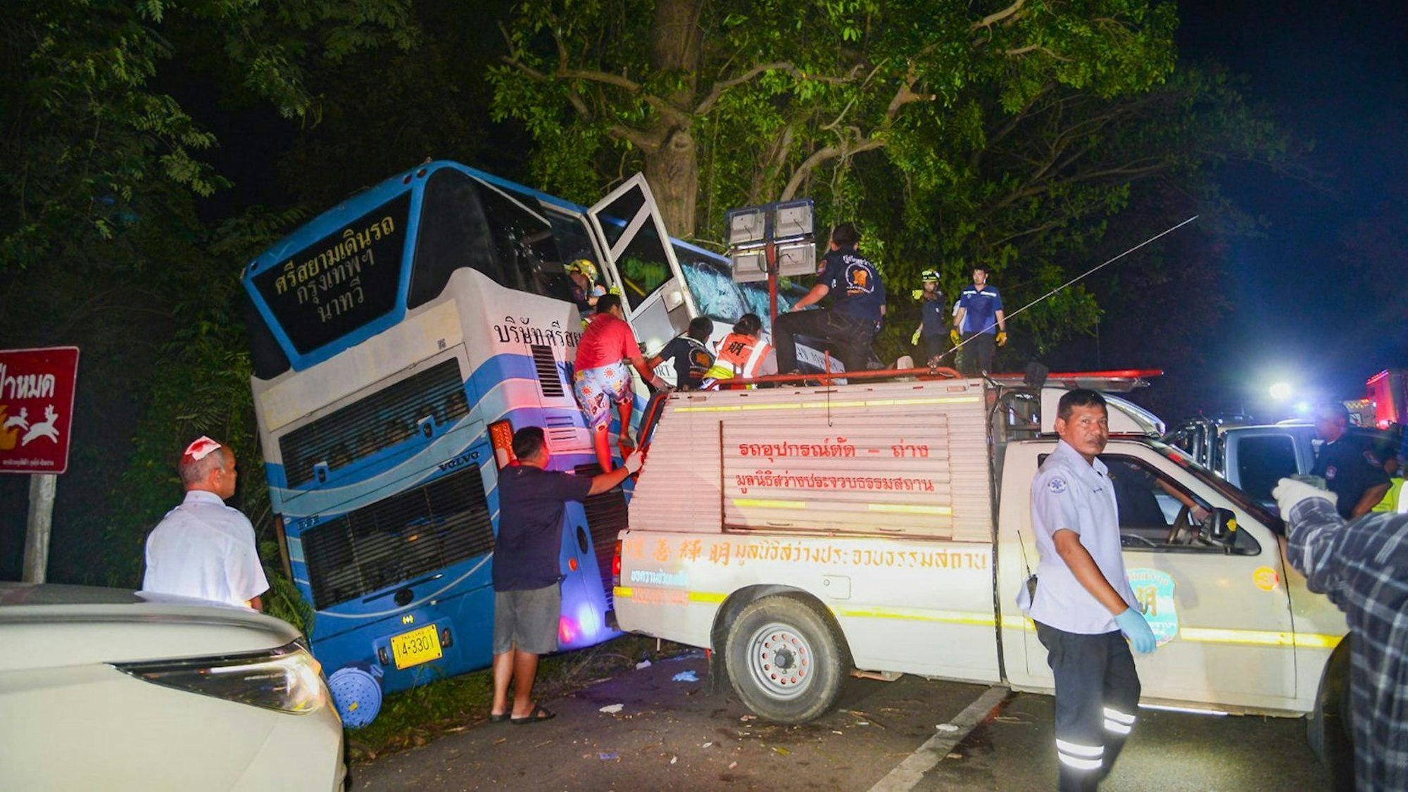 In this photo provided by Sawang Rungrueang Rescue22 Foundation, rescue workers and volunteers work at the site of a bus accident Tuesday, Dec 5, 2023, at the Prachuap Khiri Khan province, Thailand. A dozen of people were killed after the vehicle fell off the road and hit a big tree.(Sawang Rungrueang Rescue22 Foundation via AP)