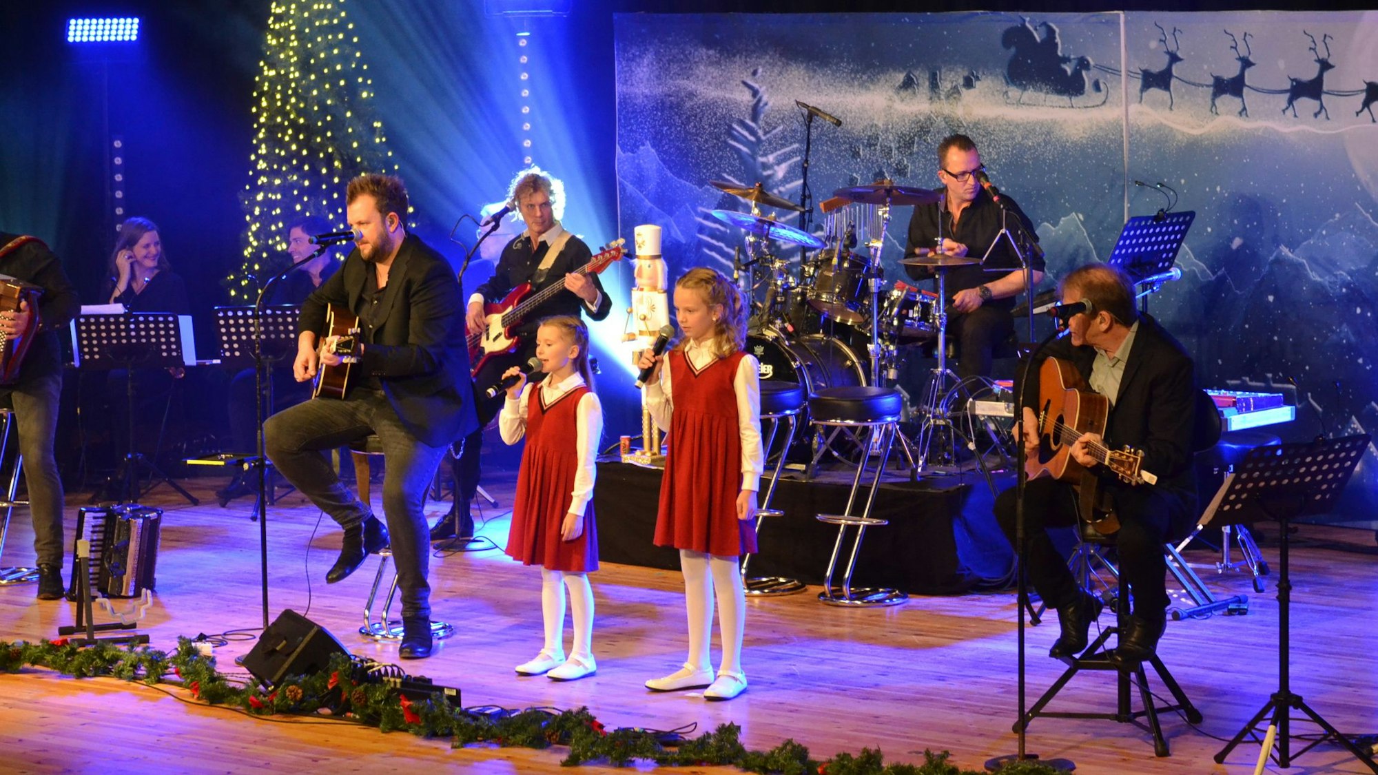 Romi und Lioli stehen in roten Kleidern mit den Paveiern auf der weihnachtlich geschmückten Bühne des Euskirchener Stadttheaters.
