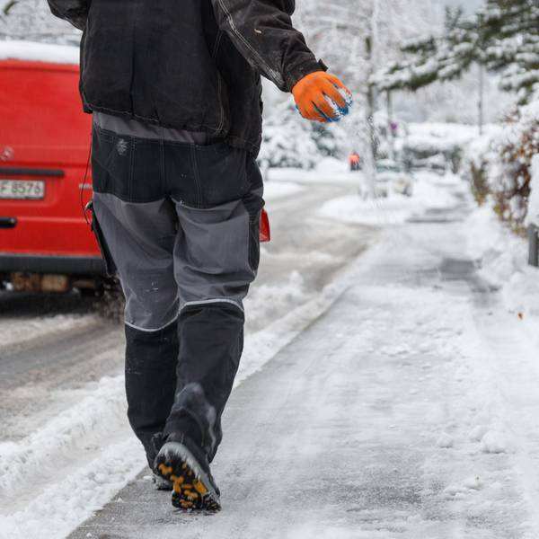 Streusalz wird von einem Mitarbeiter vom Winterdienst auf einen Gehweg gestreut.