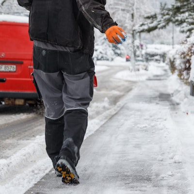 Streusalz wird von einem Mitarbeiter vom Winterdienst auf einen Gehweg gestreut.