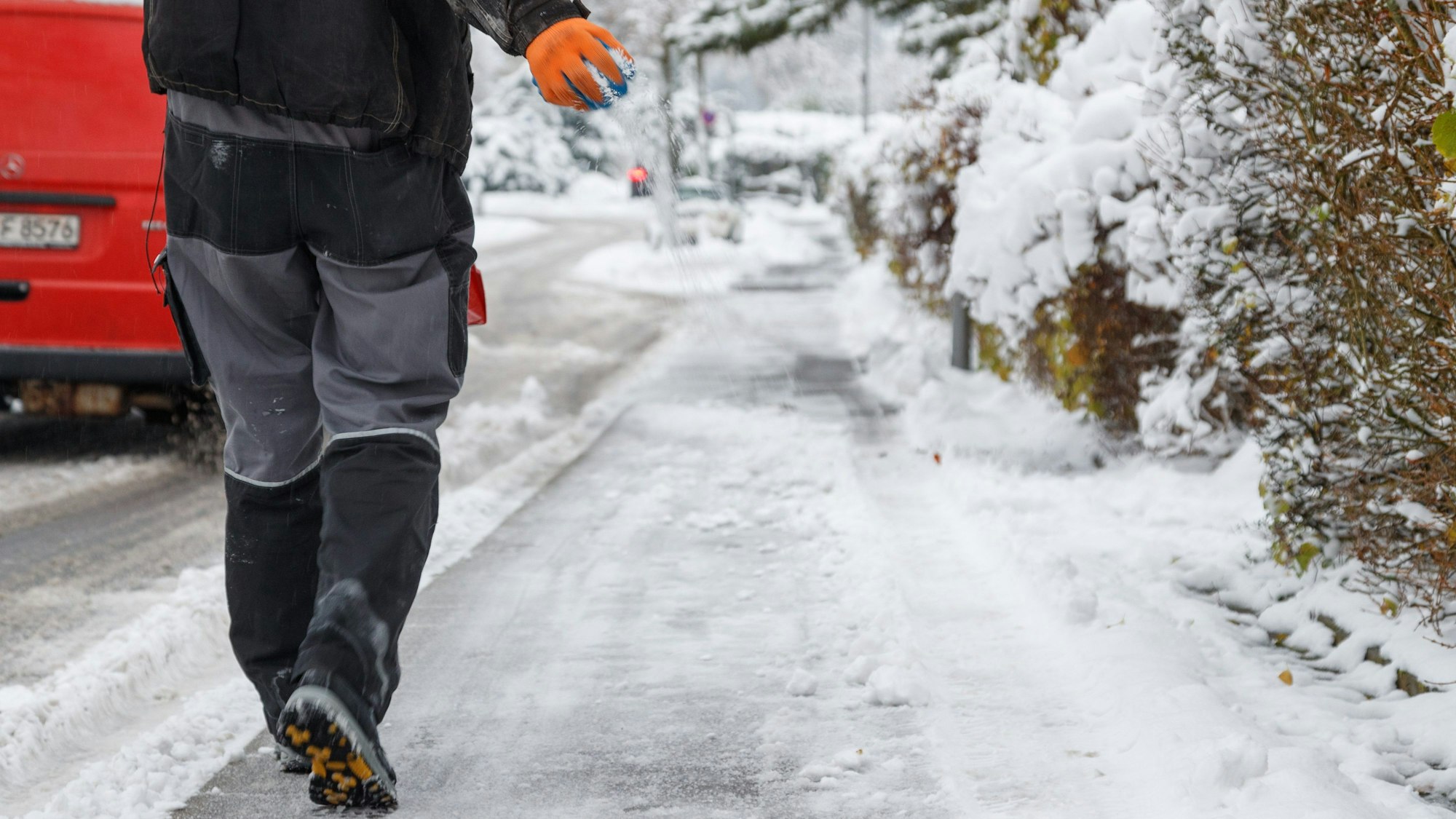 Streusalz wird von einem Mitarbeiter vom Winterdienst auf einen Gehweg gestreut.