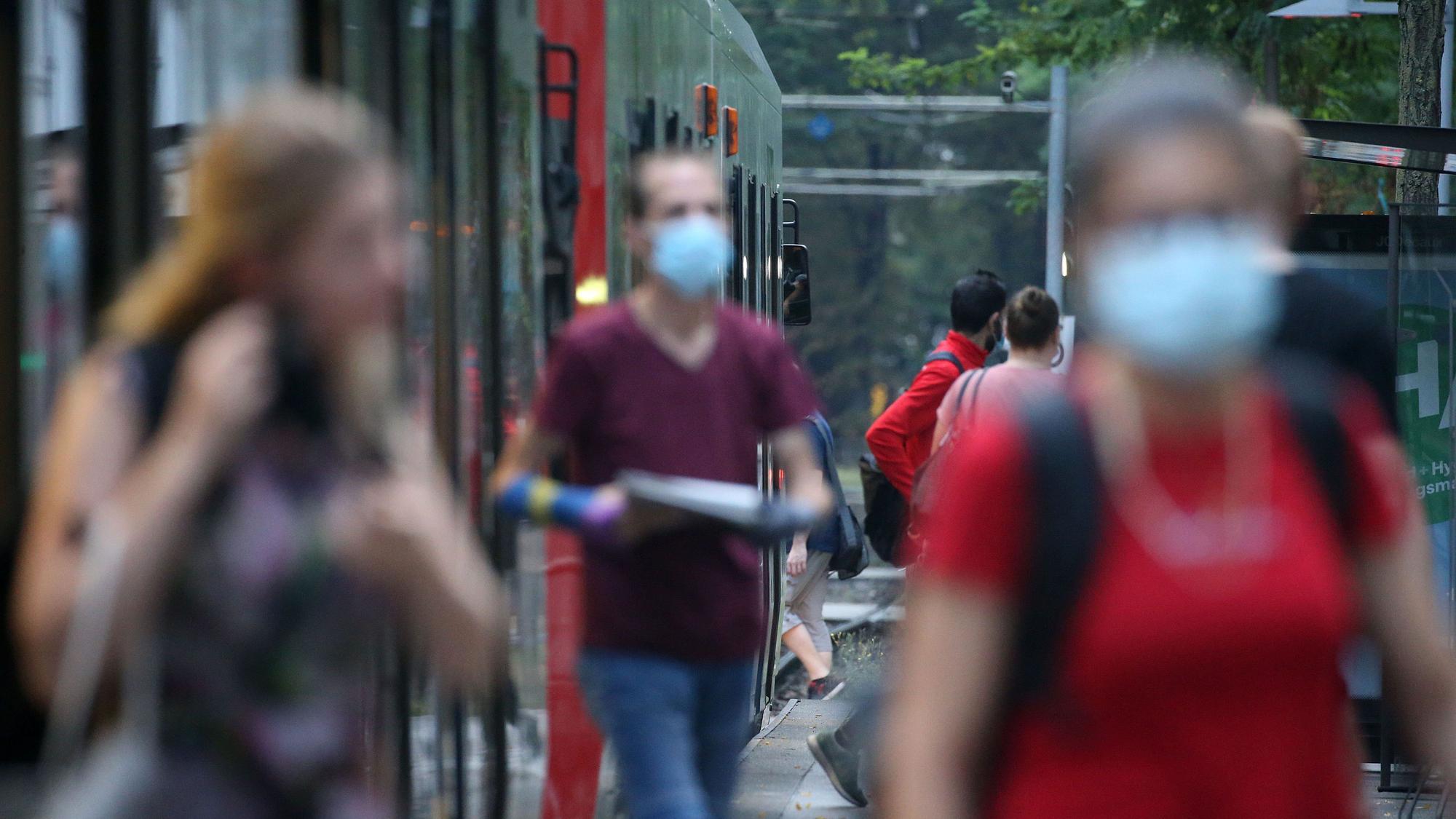 Fahrgäste verlassen mit Schutzmasken einen Bahnsteig neben einer Straßenbahn.