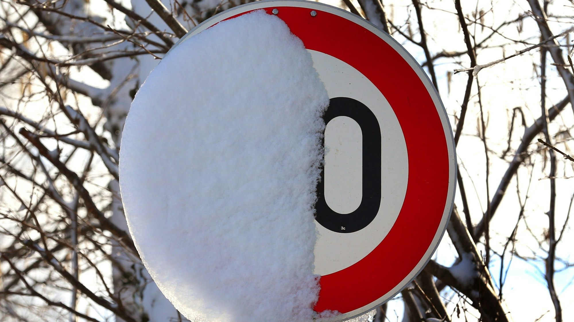 Ein Schild, das auf ein Tempolimit hinweist, ist halb zugeschneit. Die Zahl ist deshalb nicht zu erkennen.
