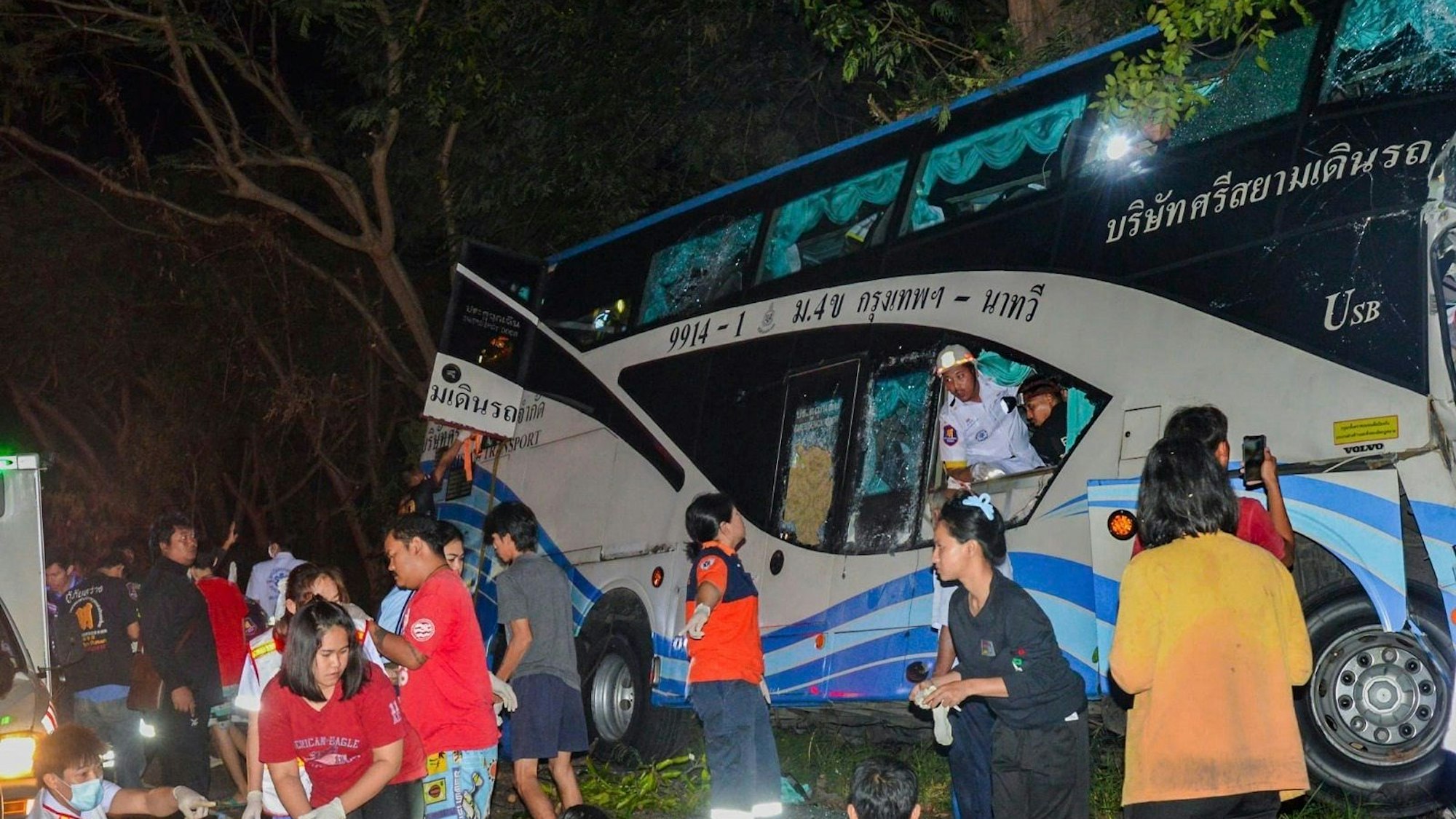 In this photo provided by Sawang Rungrueang Rescue22 Foundation, rescue workers and volunteers work at the site of a bus accident Tuesday, Dec 5, 2023, at the Prachuap Khiri Khan province, Thailand. A dozen of people were killed after the vehicle fell off the road and hit a big tree.(Sawang Rungrueang Rescue22 Foundation via AP)