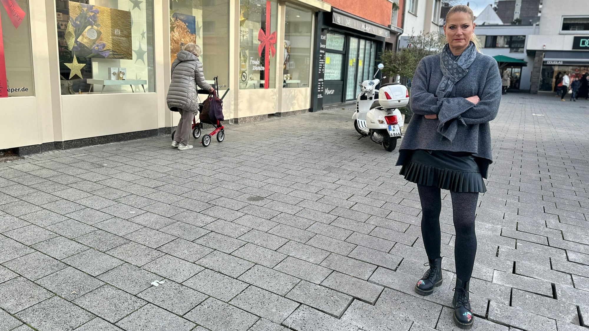 Eine Frau steht auf einem Platz, die Pflastersteine sind zum Teil schief.