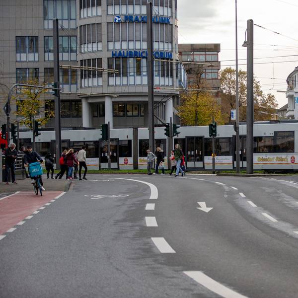 Eine Straßenbahn fährt eine leichte Kurve auf den Neumarkt zu. Fußgänger gehen über eine Straße.