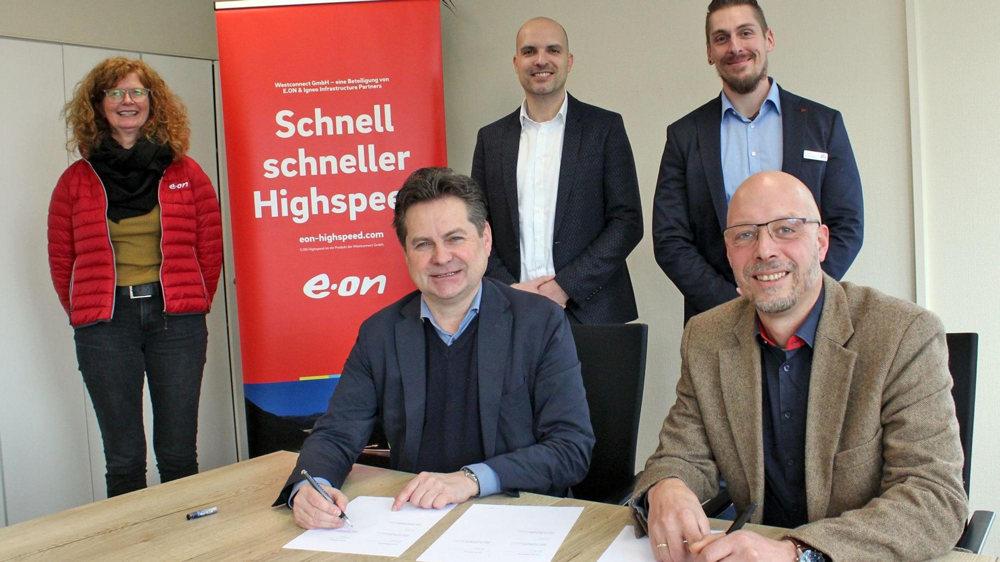 Zwei Herren am Tisch, dahinter stehend drei weitere Personen.