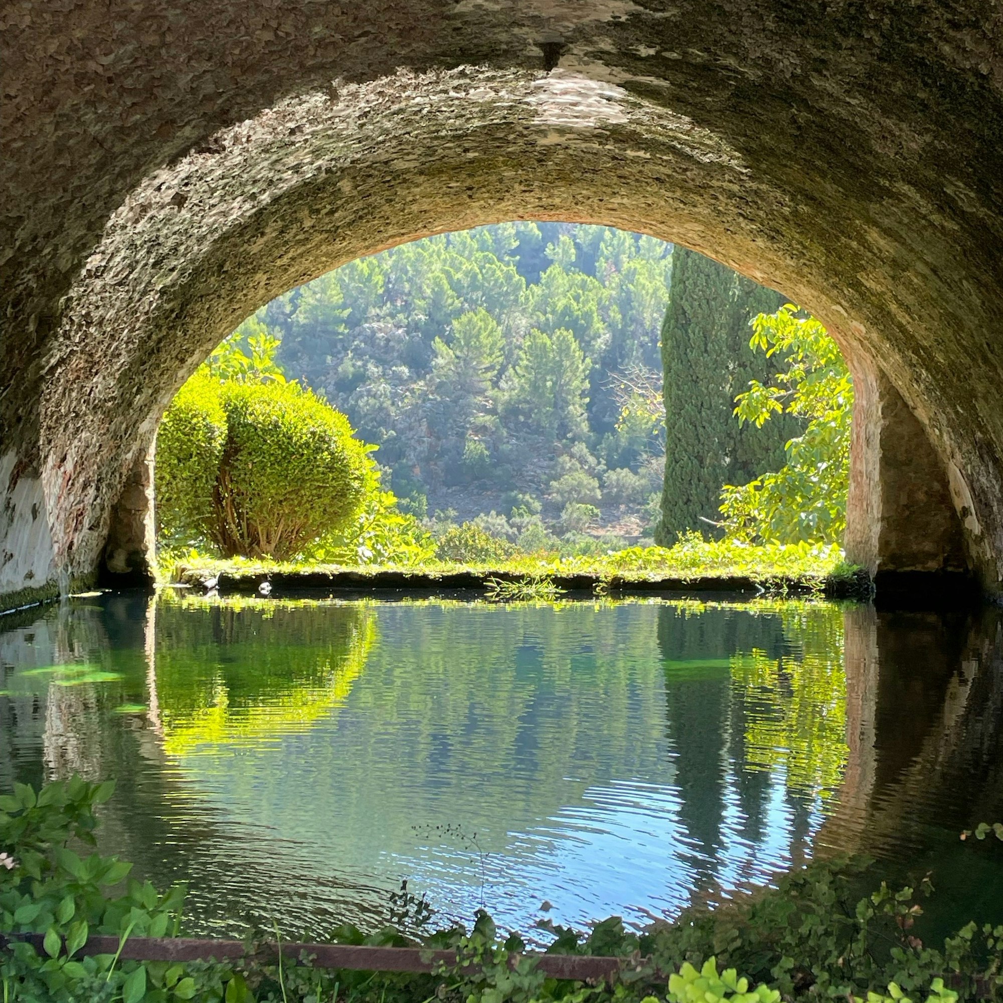 Ein Steinbogen spiegelt sich im Wasser.