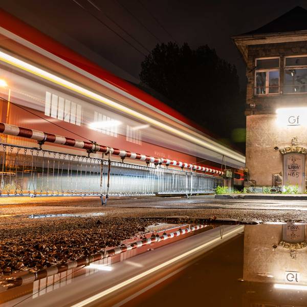 Eine Pfütze spiegelt den Bahnübergang Tannenbergstraße, durch den gerade eine S-Bahn fährt.