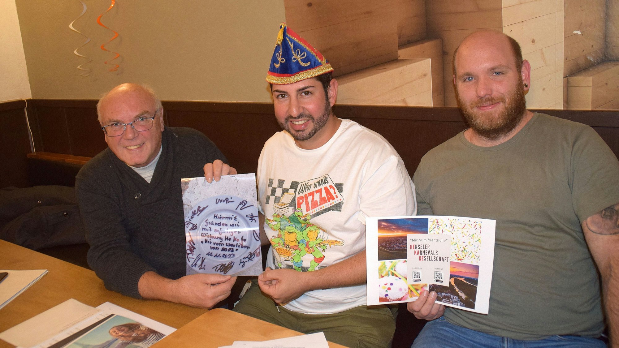 Drei Männer sitzen auf einer Bank und halten Bilder in die Kamera.