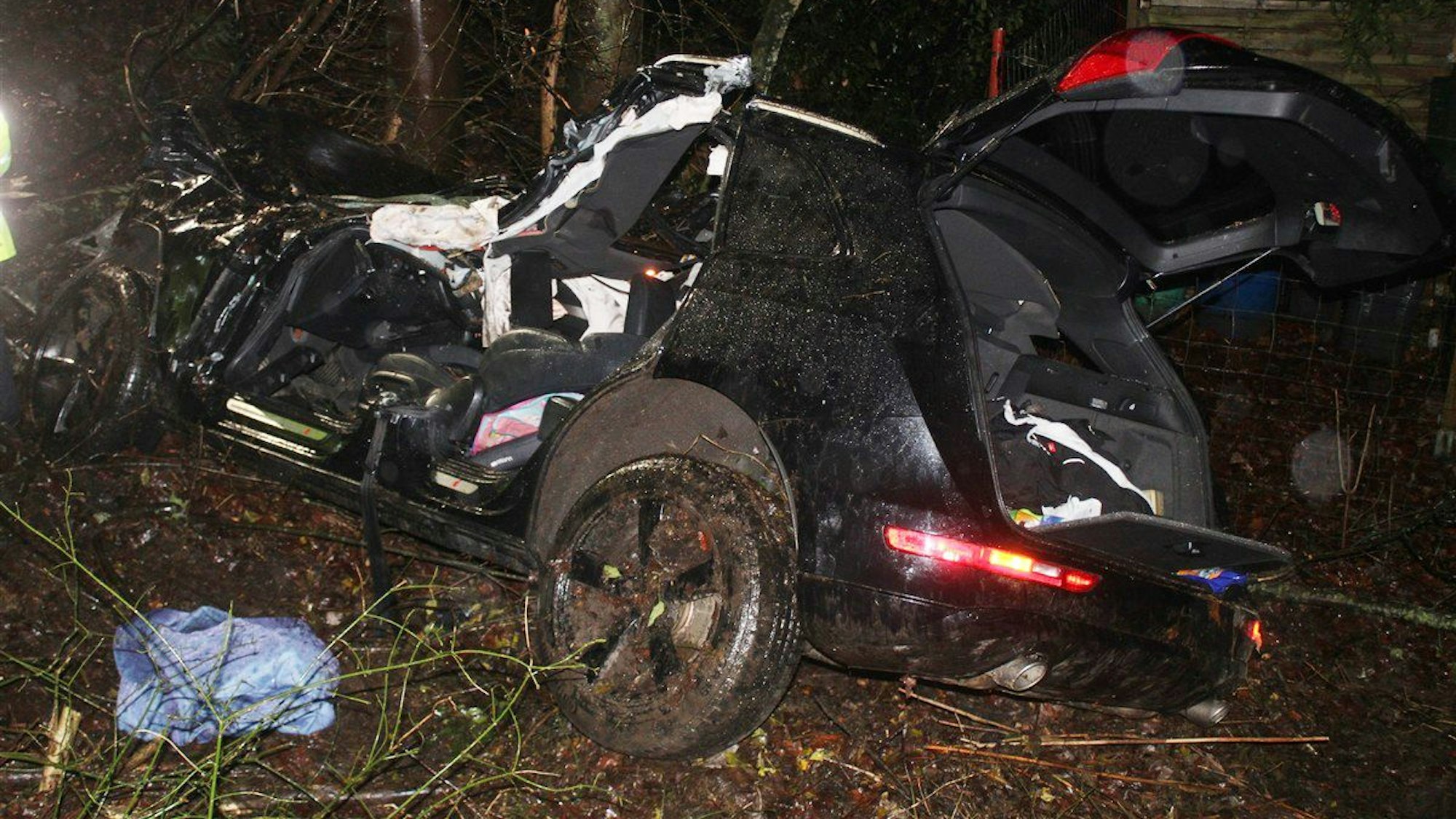Ein schwer beschädigtes Auto, das von der Feuerwehr bereits teilweise zerlegt ist, steht in der Nacht in einer Böschung.