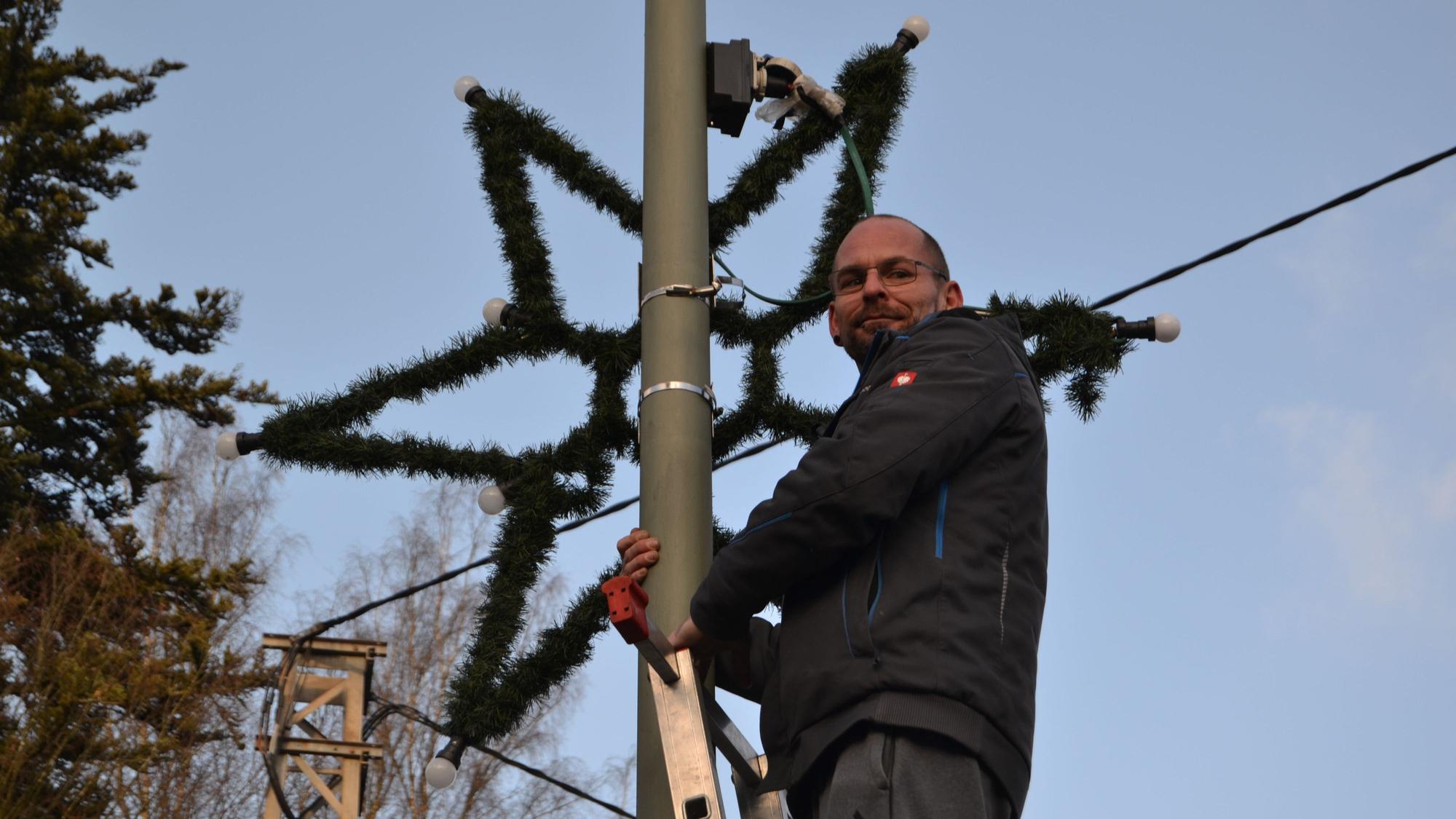 Auf einer Leiter in mehr als drei Metern Höhe steht Oliver Herrmann, der gerade einen Stern als Weihnachtsschmuck an die Straßenlaterne gehängt hat.