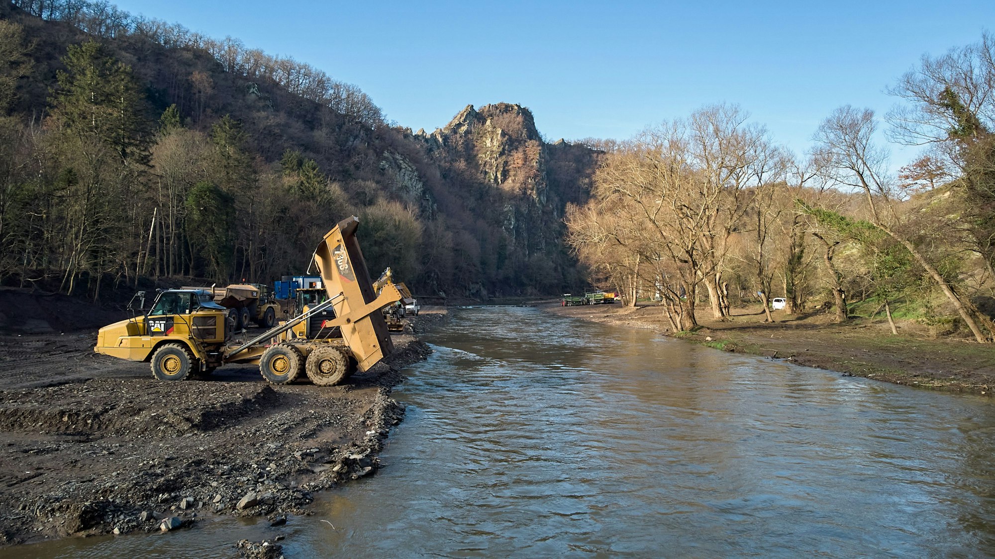 Baumaschinen stehen an der Ahrtalschleife bei Altenahr am Flussufer.