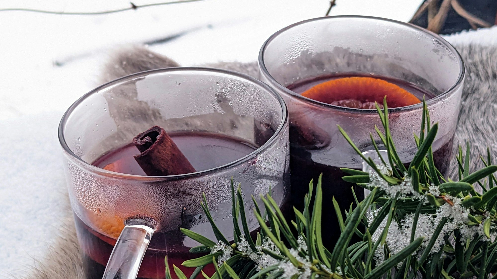 Zwei Glastassen sind mit Glühwein gefüllt. In den Gläsern sind noch Orangenscheiben und eine Stange Zimt drinnen.