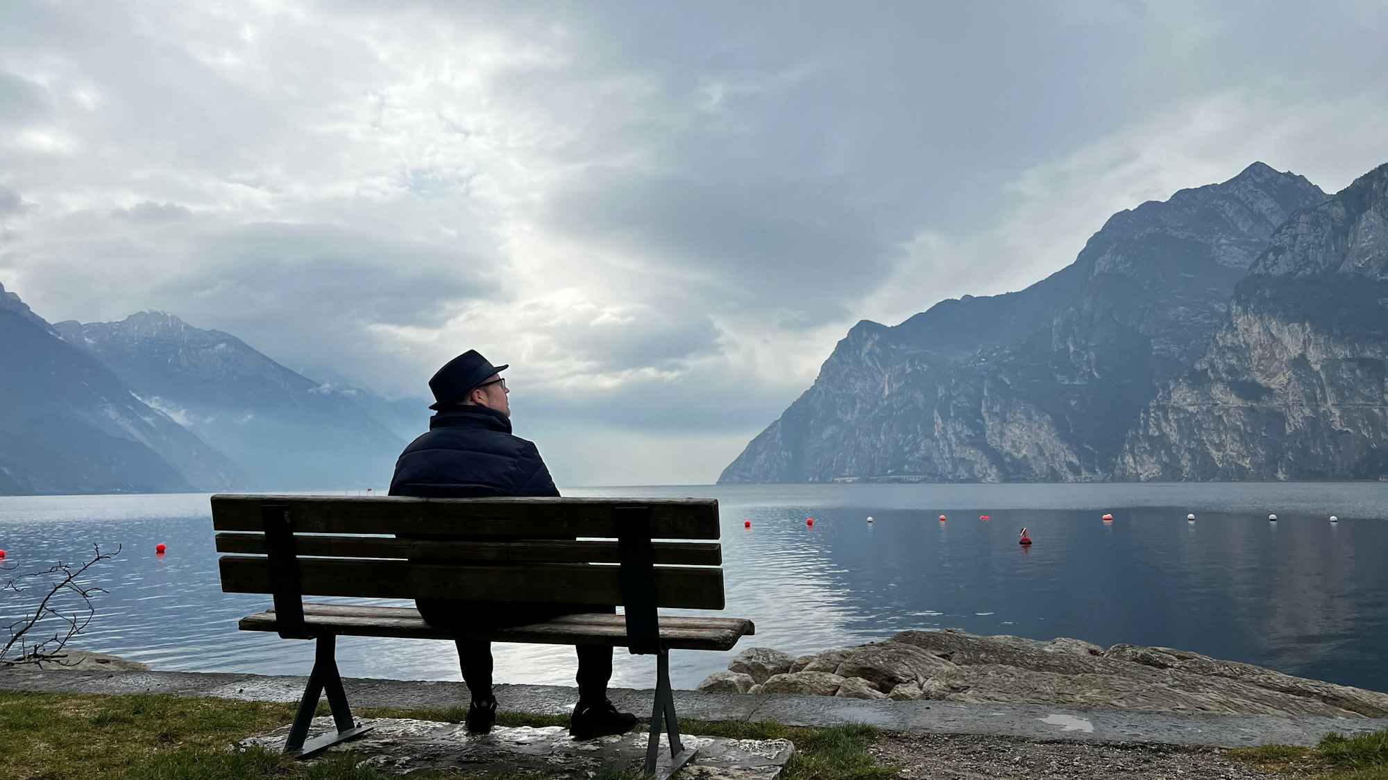 Das Tonstudio, in dem Björn Heuser das Album „Janz besinnlich“ aufnahm, lag direkt am Gardasee. Italien war das Lieblings-Urlaubsland seiner Eltern, denen das Album gewidmet ist. Das Foto zeigt Heuser auf einer Bank sitzend mit Blick auf den See und in die dahinter liegenden Berge.