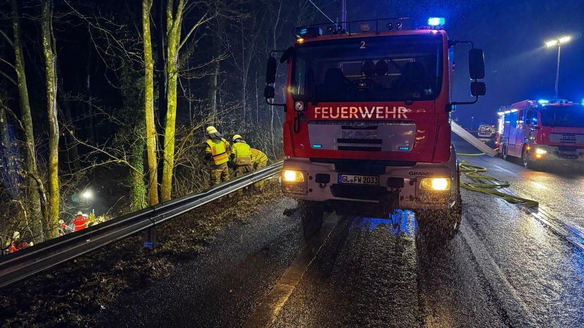 Feuerwehrautos stehen auf der Overather Straße, Feuerwehrleute arbeiten in der Böschung neben der Straße.