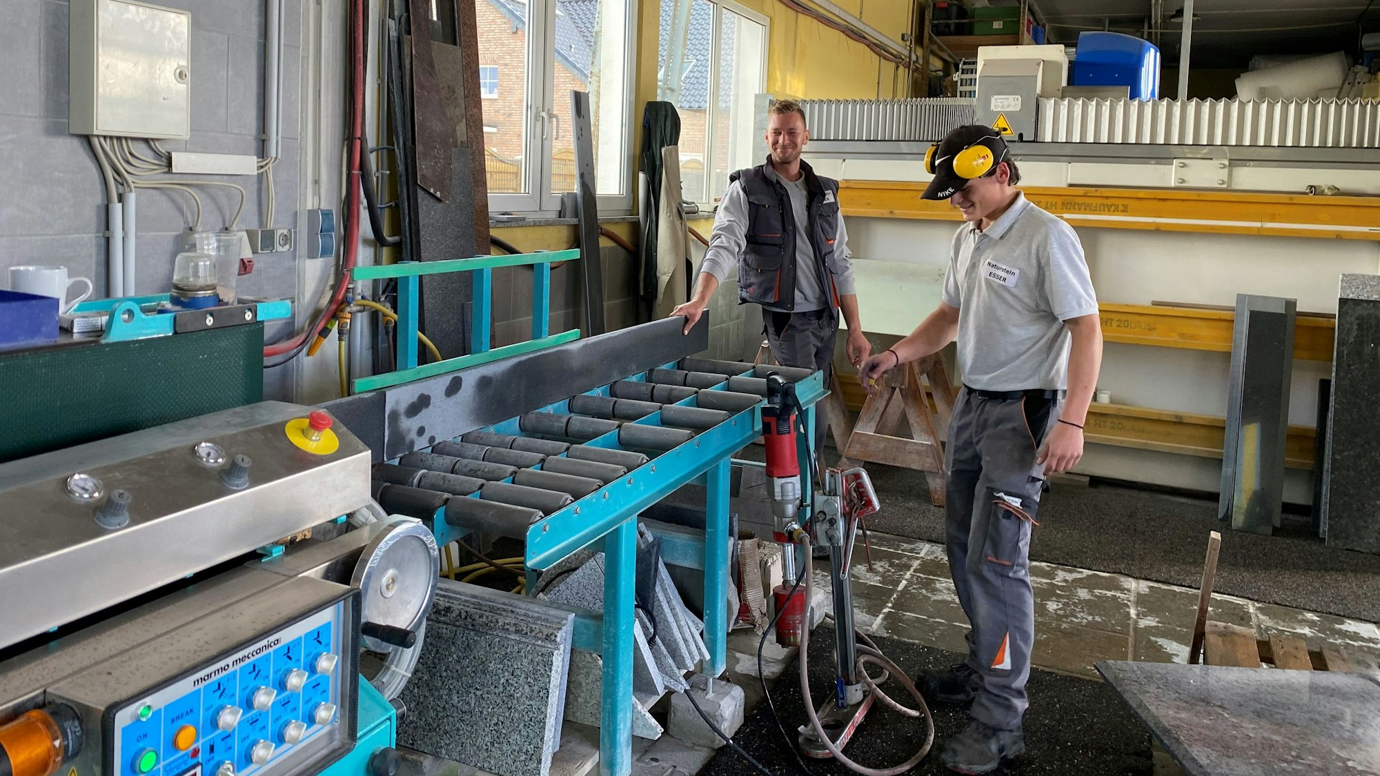 Zwei Mitarbeiter schieben eine Steinplatte in eine Maschine.