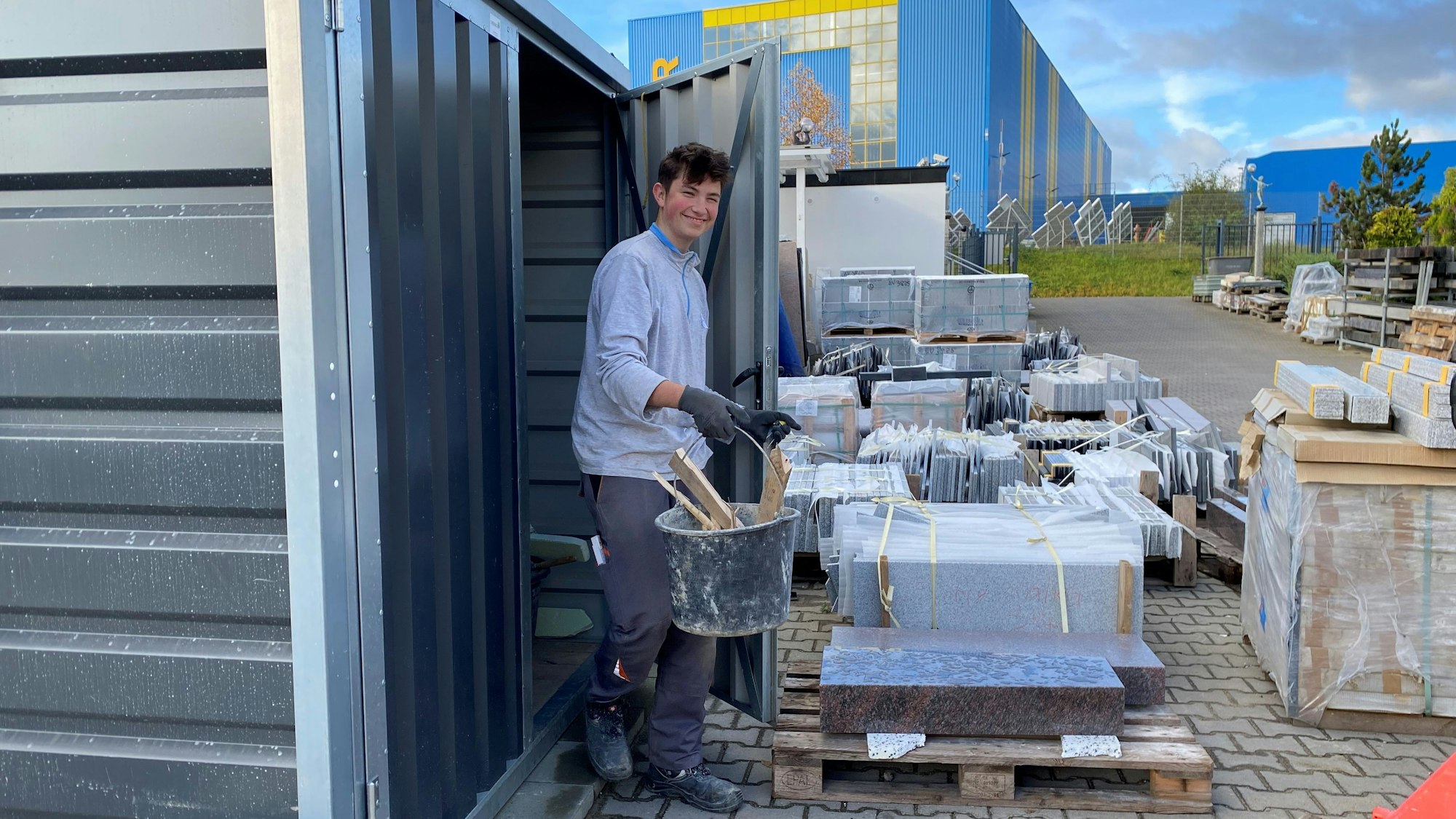 Der Auszubildende Benjamin Achnik kommt mit einem Eimer voll Holz aus einem Schuppen.