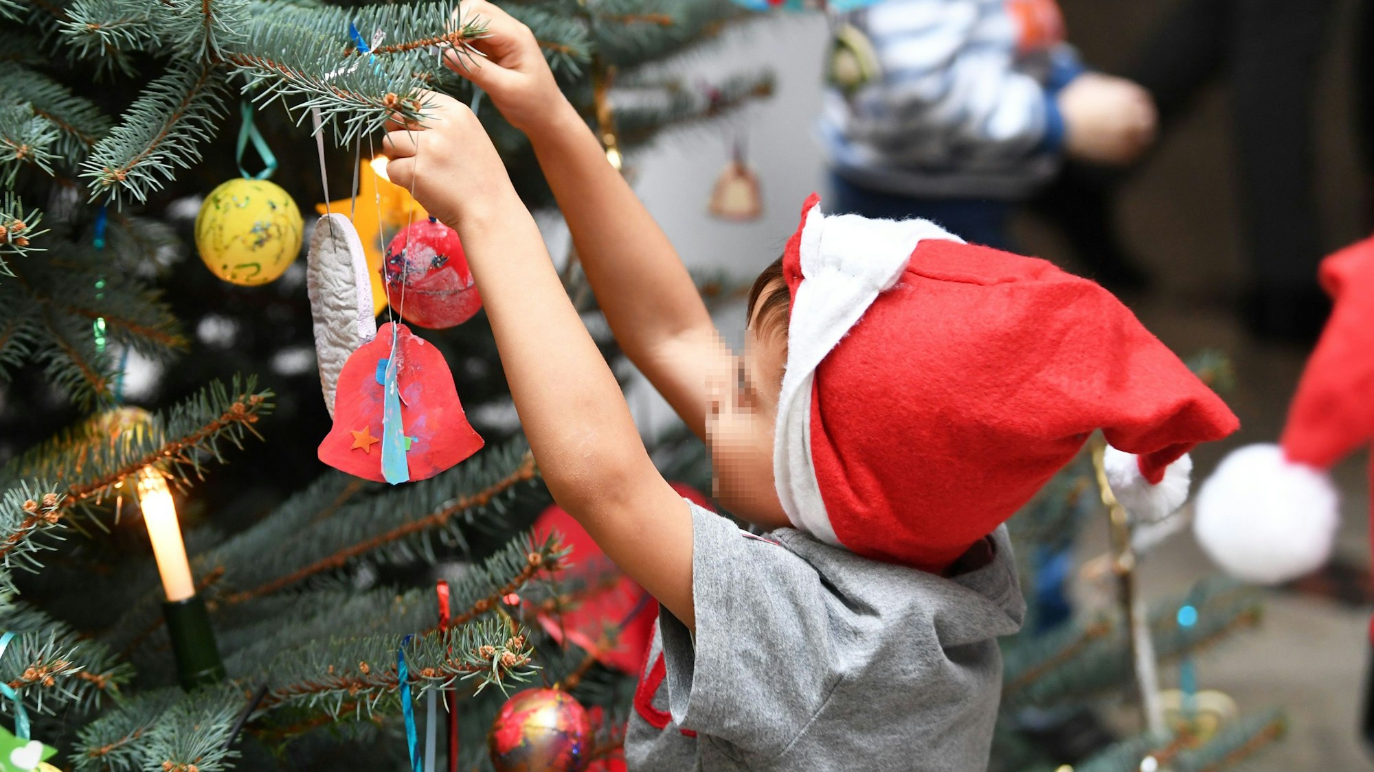 Ein Kind an einem Weihnachtsbaum. Der Verzicht einer Kita auf einen Weihnachtsbaum hatte hohe Wellen geschlagen, nun sprach der Kita-Träger von Drohungen. (Symbolbild)