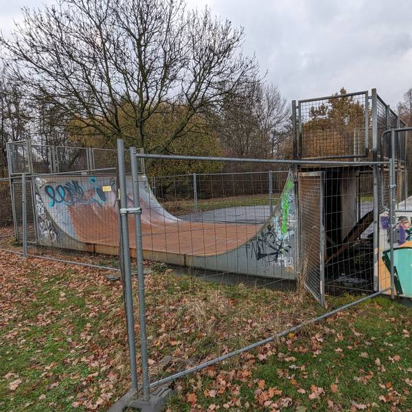 Eine mit Graffiti versehene Halfpipe für Skater hinter einem Bauzaun.