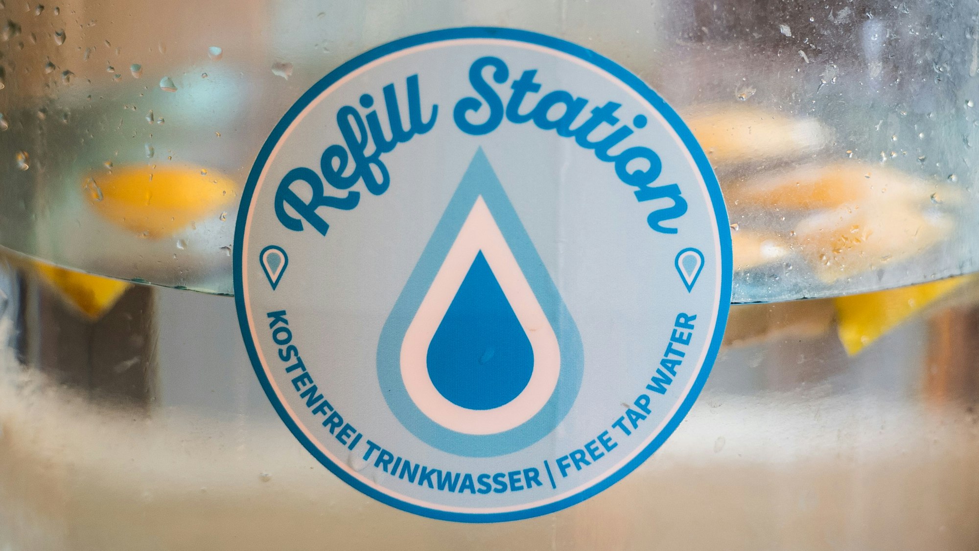 Auf dem Foto ist der Aufkleber „Refill-Station“ zu sehen. Er weist auf die kostenlose Abgabe von Trinkwasser hin.